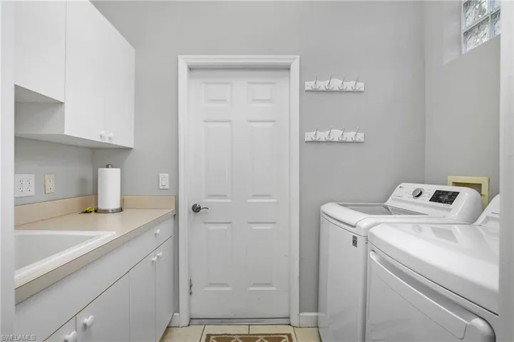 Laundry area featuring light tile patterned flooring, cabinets, sink, and washer and dryer