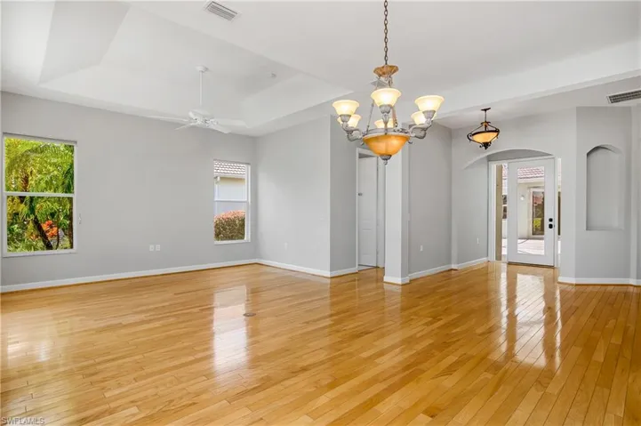 Unfurnished room featuring ceiling fan with notable chandelier, a tray ceiling, and light hardwood / wood-style floors