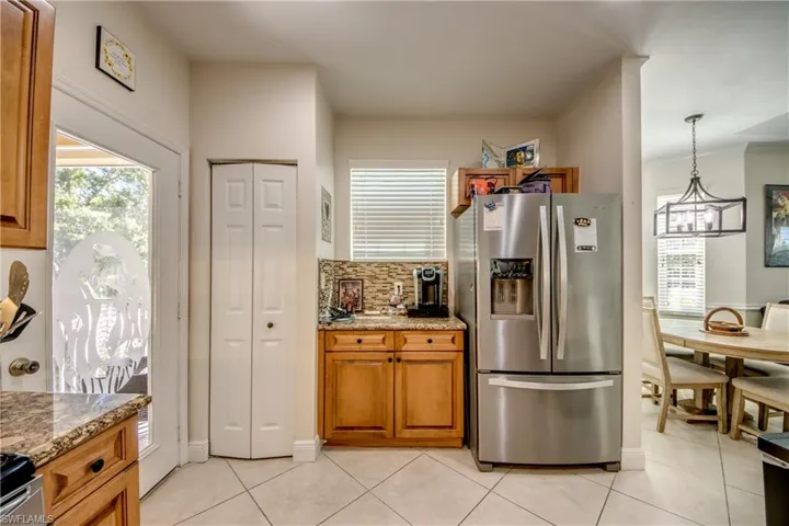 Kitchen with stainless steel fridge with ice dispenser, decorative backsplash, brown cabinets, light stone countertops, and light tile patterned floors