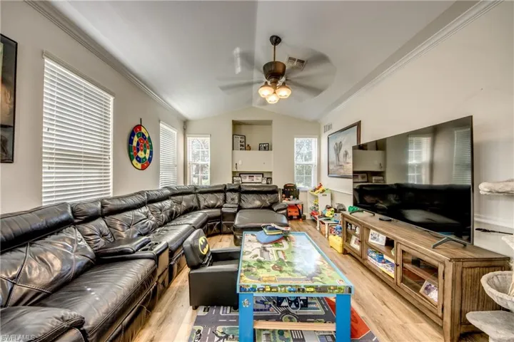 Living area featuring crown molding, lofted ceiling, light wood-type flooring, and a ceiling fan
