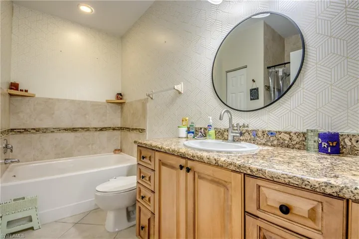 Full bath featuring light tile patterned floors, tile walls, vanity, a garden tub, and tasteful backsplash