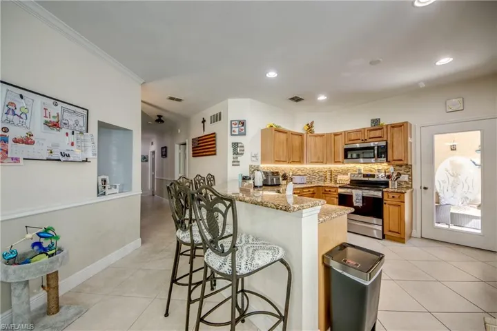 Kitchen with stainless steel appliances, decorative backsplash, light stone countertops, a peninsula, and light tile patterned floors