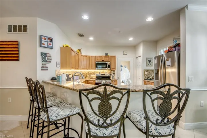 Kitchen featuring backsplash, light tile patterned floors, appliances with stainless steel finishes, dark stone countertops, and recessed lighting