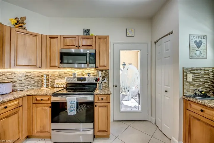 Kitchen featuring decorative backsplash, appliances with stainless steel finishes, light stone counters, light tile patterned floors, and brown cabinetry