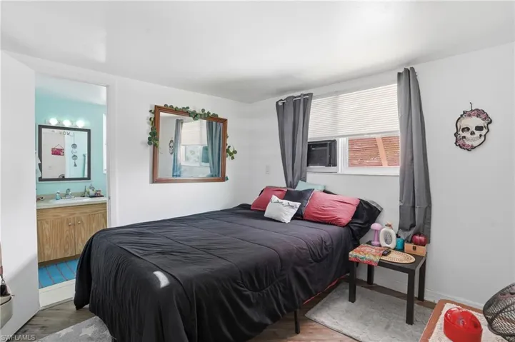 Bedroom featuring wood finished floors, multiple windows, ensuite bathroom, and cooling unit - Virtually Edited Image