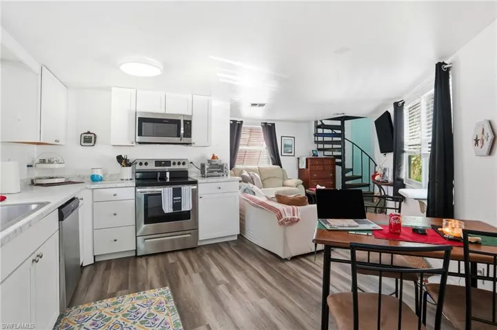 Kitchen featuring white cabinets, appliances with stainless steel finishes, light countertops, dark wood-style floors, and open floor plan