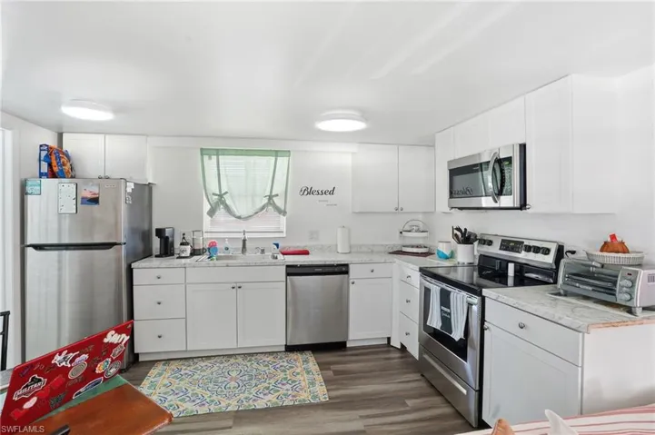 Kitchen featuring appliances with stainless steel finishes, light countertops, white cabinetry, and dark wood-type flooring - Virtually Edited Image