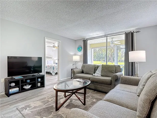 Living area with ceiling fan, wood finished floors, and a textured ceiling