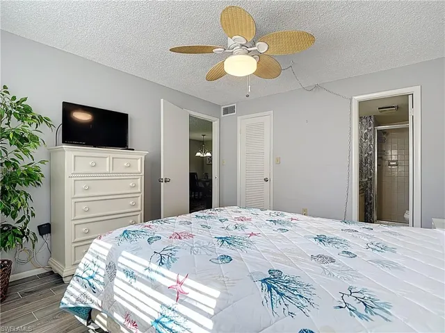 Bedroom with a textured ceiling, wood tiled floors, ceiling fan, and connected bathroom