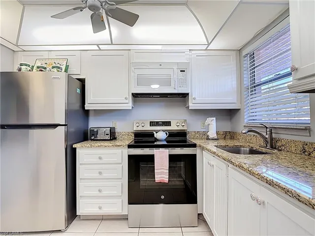 Kitchen featuring appliances with stainless steel finishes, white cabinets, light stone countertops, light tile patterned floors, and a ceiling fan