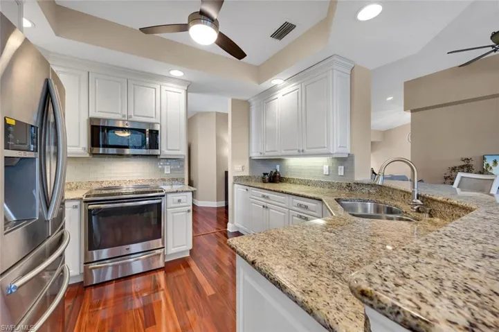 Kitchen featuring sink, dark hardwood / wood-style floors, light stone countertops, appliances with stainless steel finishes, and white cabinetry