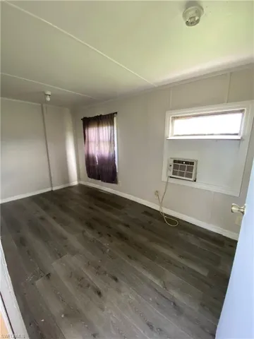 Unfurnished room with dark hardwood / wood-style floors and an AC wall unit