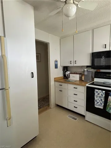 Kitchen with a ceiling fan, wood looking counters and white cabinetry