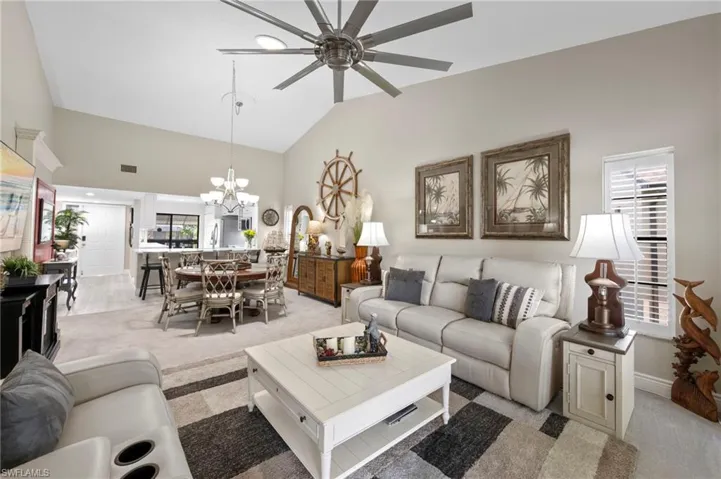 Living area featuring light carpet, a ceiling fan, high vaulted ceiling, and a chandelier