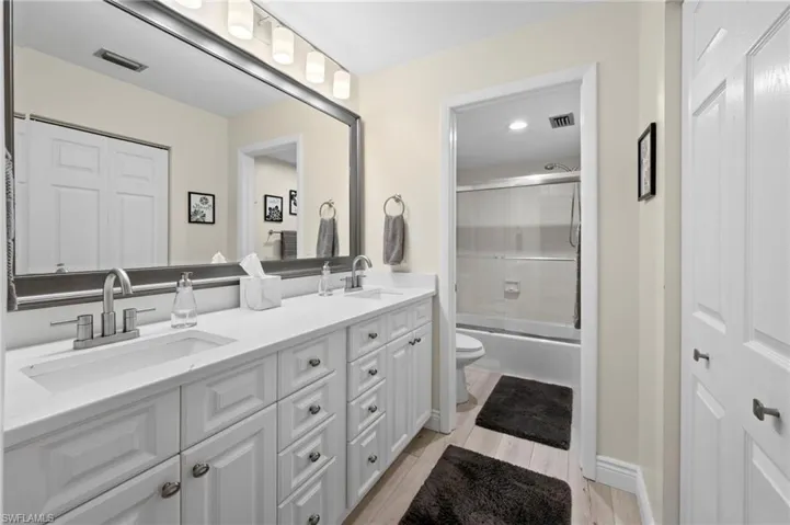Full bathroom featuring toilet, double vanity, enclosed tub / shower combo, and wood finished floors