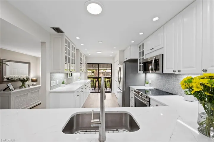 Kitchen with stainless steel appliances, decorative backsplash, a sink, recessed lighting, and light stone countertops