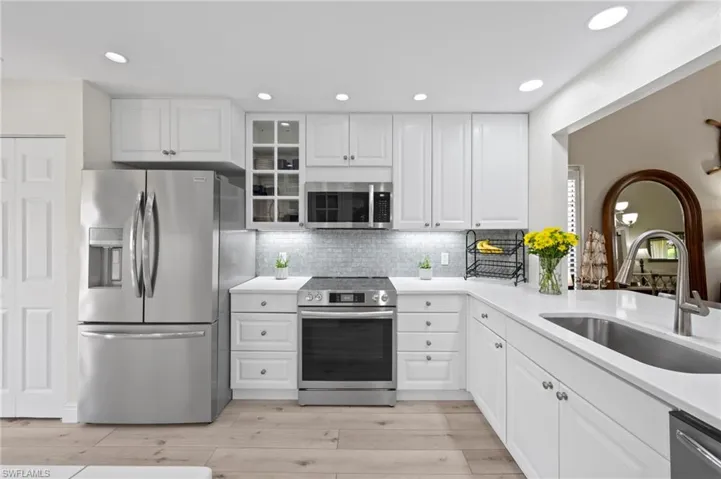 Kitchen with stainless steel appliances, a sink, backsplash, light wood-style floors, and glass insert cabinets