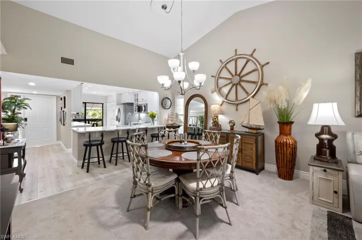 Dining room featuring light colored carpet, baseboards, a chandelier, and high vaulted ceiling