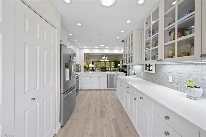 Kitchen featuring appliances with stainless steel finishes, white cabinets, light wood finished floors, tasteful backsplash, and glass insert cabinets