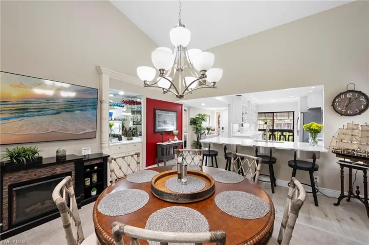 Dining area featuring a chandelier, light wood finished floors, a glass covered fireplace, high vaulted ceiling, and ornate columns