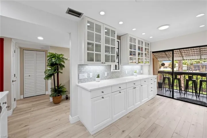 Kitchen with light wood-style flooring, backsplash, light countertops, glass insert cabinets, and recessed lighting