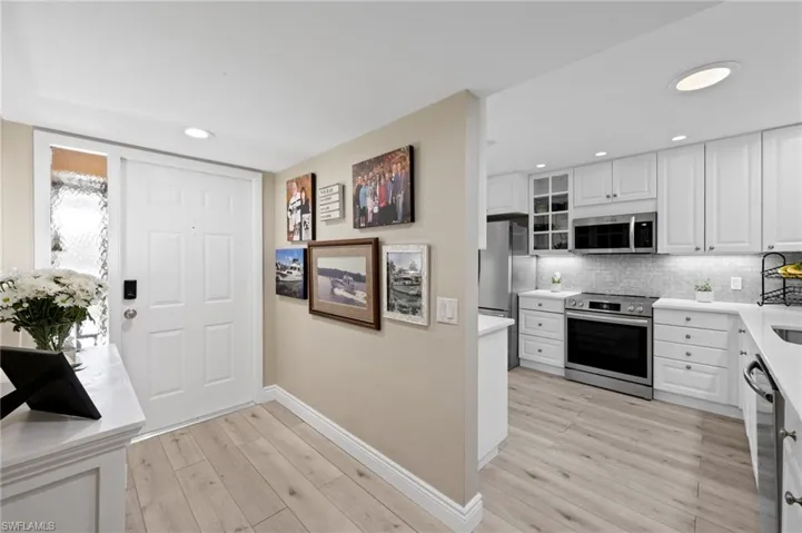 Kitchen with stainless steel appliances, baseboards, light wood-type flooring, backsplash, and white cabinets
