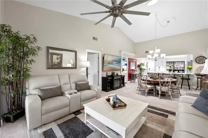 Living area with high vaulted ceiling, ceiling fan, light colored carpet, and a chandelier