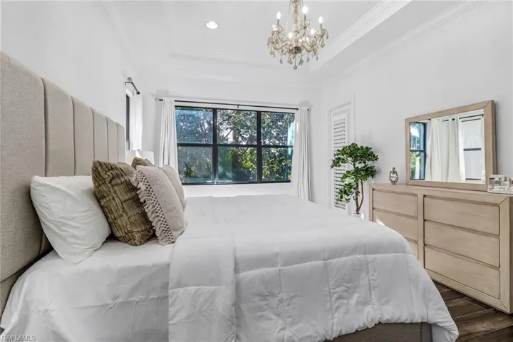 Bedroom featuring multiple windows, a chandelier, dark wood finished floors, crown molding, and a raised ceiling