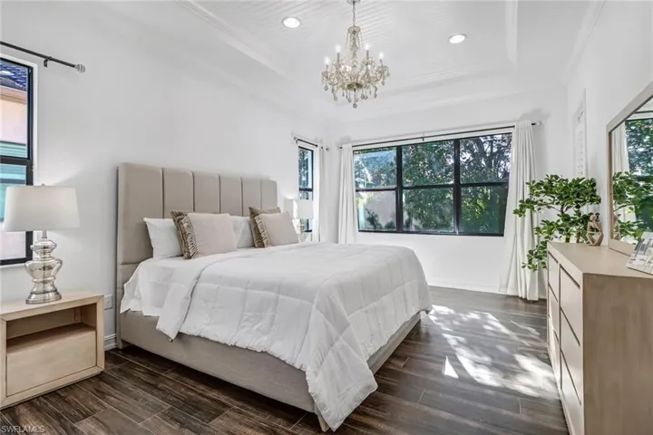 Bedroom featuring a raised ceiling, dark wood-style floors, a chandelier, and ornamental molding