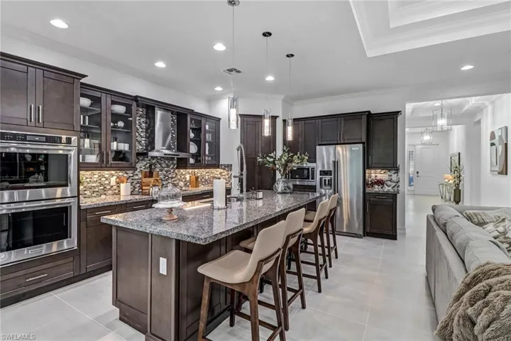 Kitchen featuring a breakfast bar area, stainless steel appliances, an island with sink, backsplash, and dark stone countertops