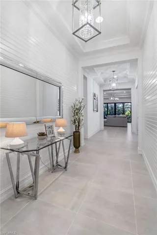 Corridor featuring suspended lighting, ornamental molding, and a raised ceiling