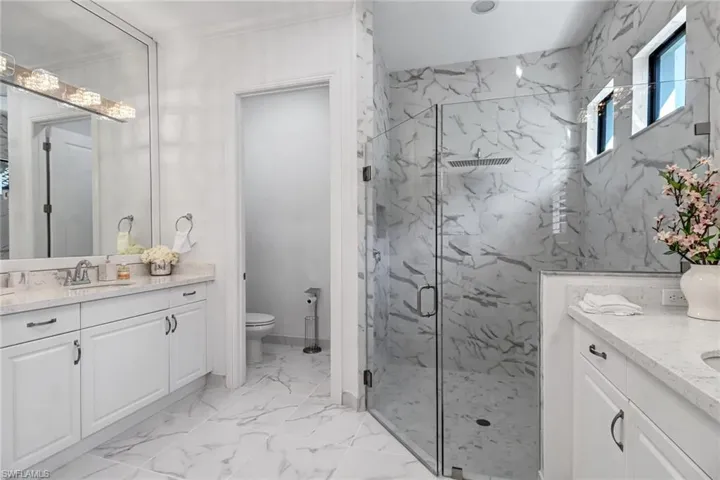 Bathroom featuring vanity, a marble finish shower, and light marble finish flooring