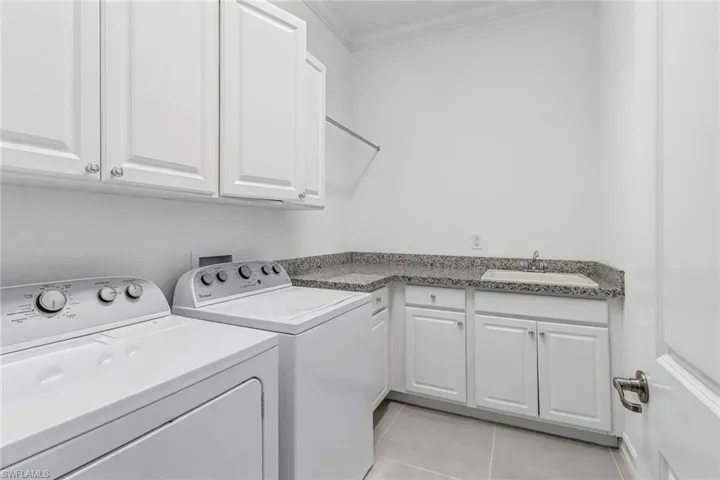 Laundry area featuring crown molding, cabinet space, washing machine and dryer, and light tile patterned flooring