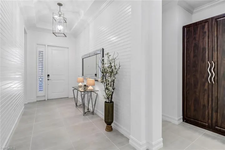 Foyer entrance with crown molding, a chandelier, a raised ceiling, and light tile patterned floors