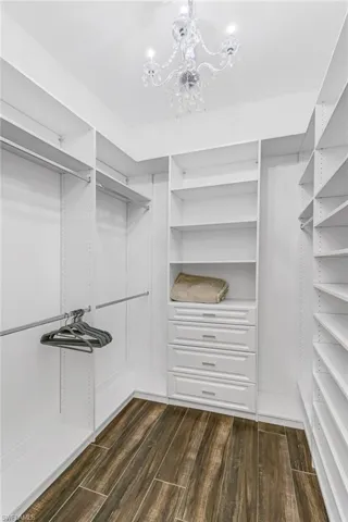Walk in closet with dark wood finished floors and suspended lighting