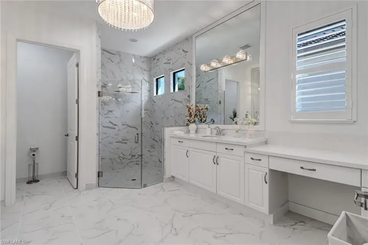Bathroom featuring a marble finish shower, vanity, hanging lights, and light marble finish floors