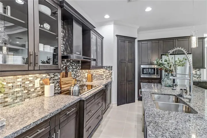 Kitchen featuring glass insert cabinets, light stone counters, pendant lighting, stainless steel appliances, and dark wood finish cabinetry