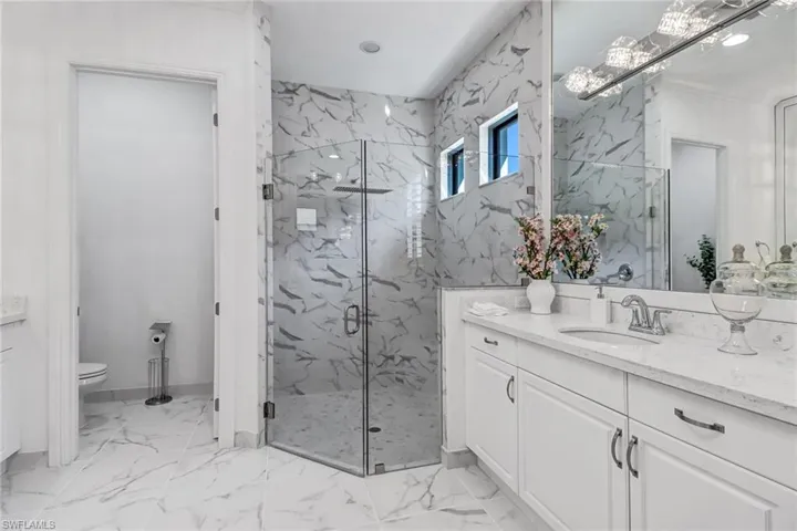 Bathroom featuring vanity, a marble finish shower, light marble finish floors, and recessed lighting