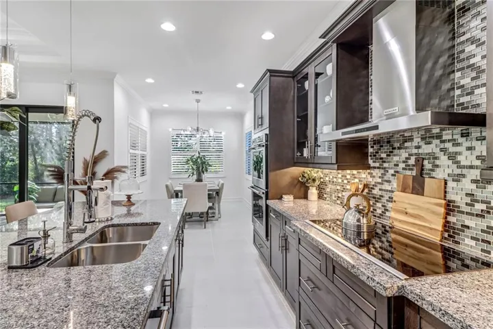 Kitchen with black electric stovetop, glass insert cabinets, light stone countertops, ornamental molding, and tasteful backsplash