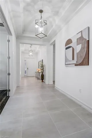 Corridor with suspended lighting, a tray ceiling, and crown molding