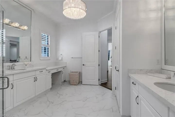 Bathroom featuring two vanities, crown molding, hanging lights, and light marble finish floors