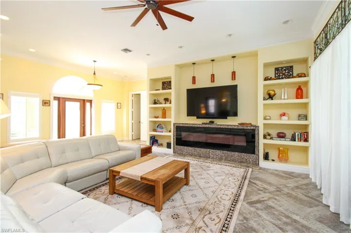 Carpeted living room featuring ornamental molding, built in features, and ceiling fan