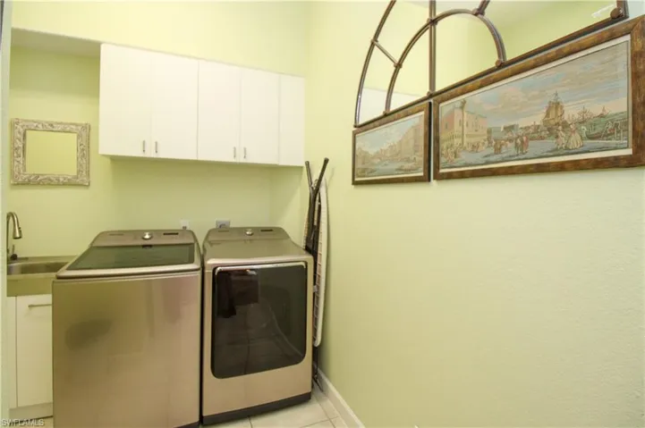 Clothes washing area with separate washer and dryer, cabinets, sink, and light tile patterned floors