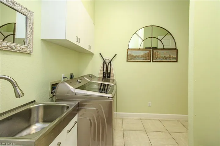 Clothes washing area featuring washing machine and dryer, cabinets, sink, and light tile patterned floors