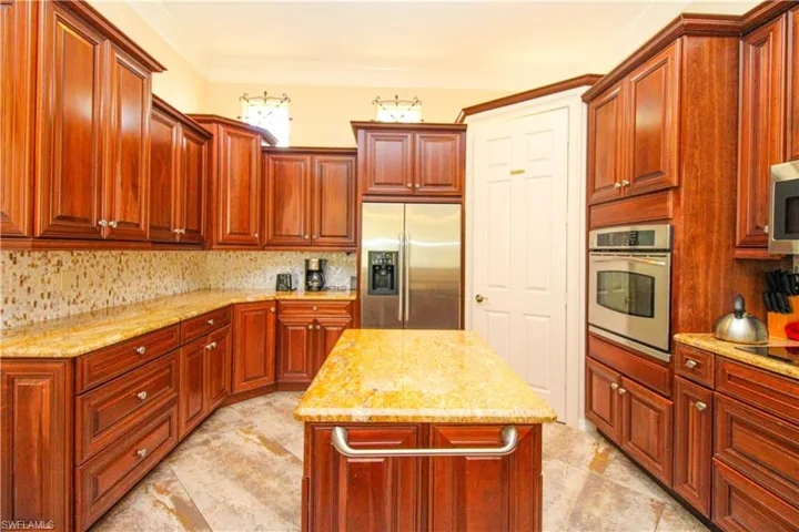 Kitchen with stainless steel appliances, light stone counters, tasteful backsplash, ornamental molding, and a center island