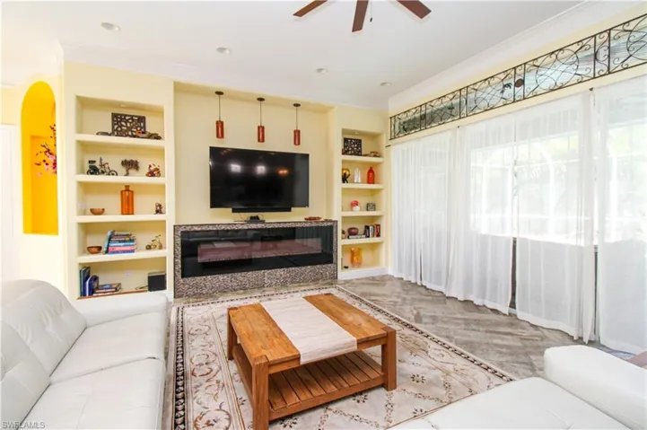 Living room featuring built in shelves, ceiling fan, and crown molding
