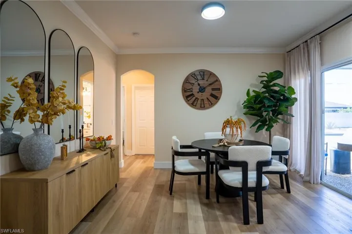 Dining room with light wood-type flooring, arched walkways, and ornamental molding