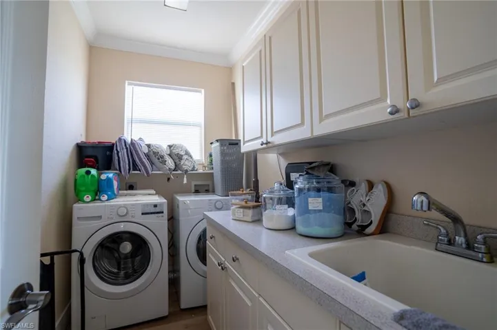 Laundry area with crown molding, washing machine and dryer, cabinet space, and dark wood-style flooring
