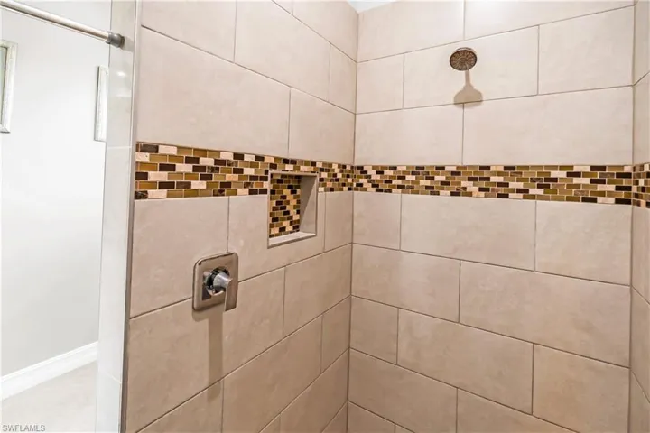 Tiled shower enclosure featuring a mosaic accent band, recessed niche, and a fixed showerhead with a single handle control