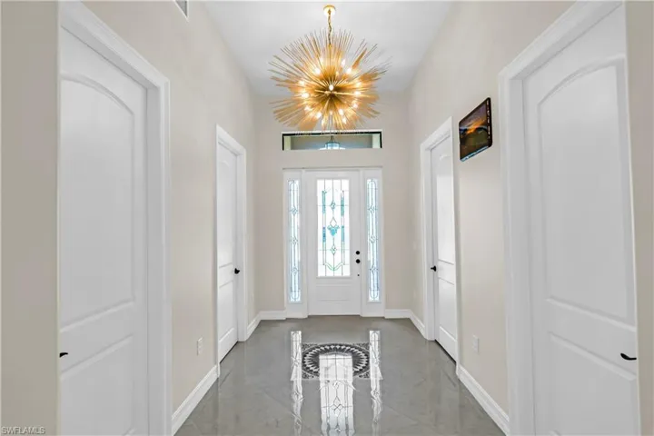 Entryway featuring glossy gray tile flooring, a decorative inlaid floor medallion, and a prominent sputnik-style chandelier